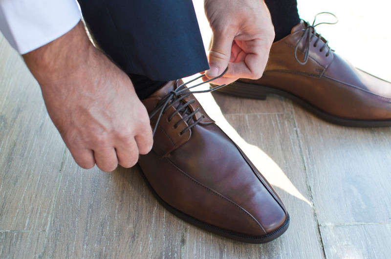 Brown leather shoes laced on a wooden floor, navy trousers.