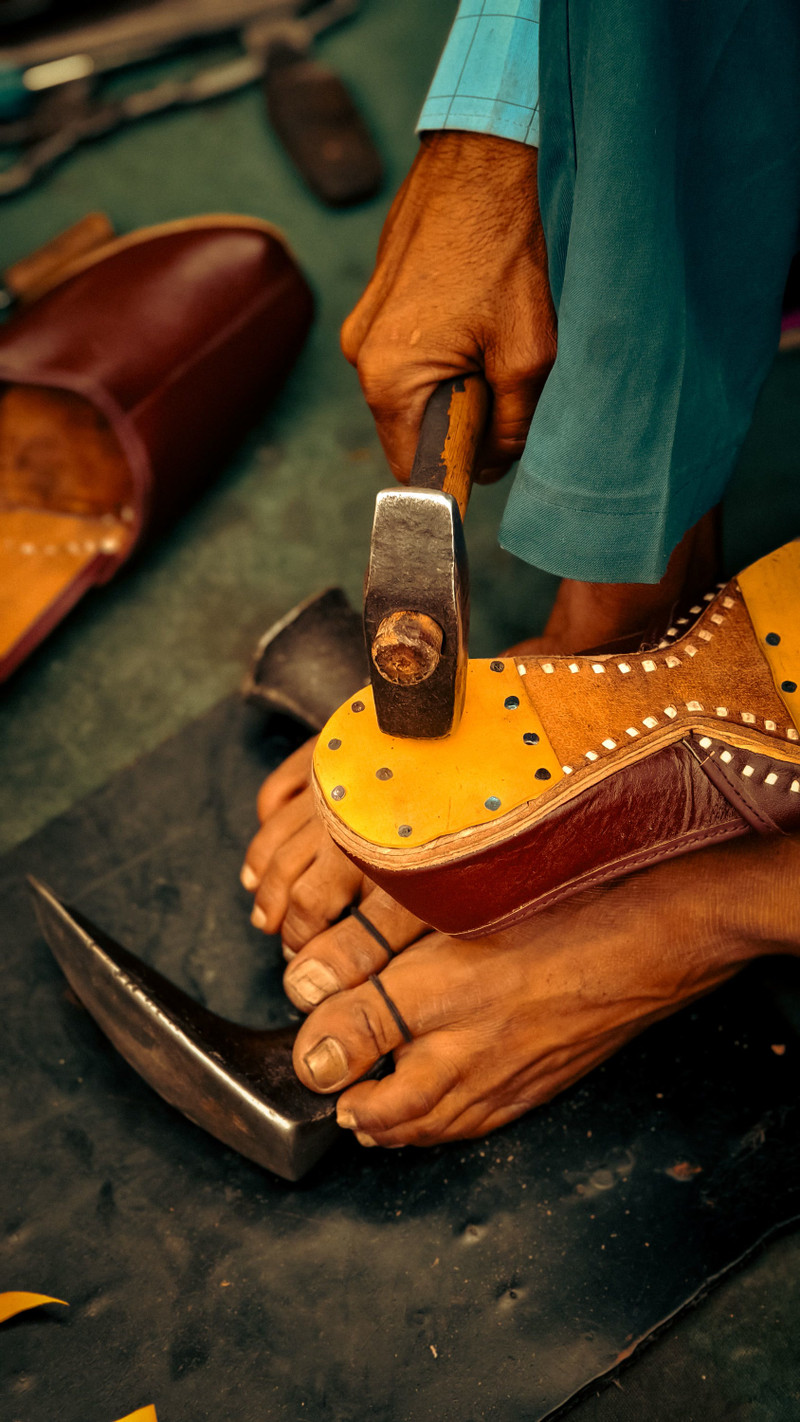 A shoemaker shaping leather with a hammer.
